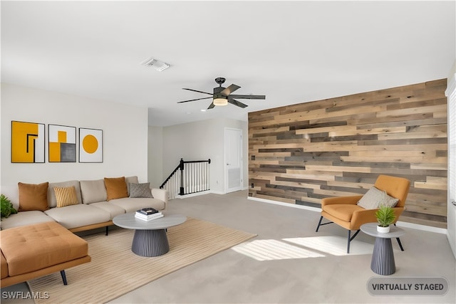 carpeted living room featuring wooden walls and ceiling fan