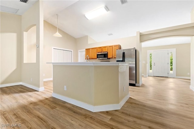 kitchen with light wood finished floors, a kitchen island with sink, light countertops, appliances with stainless steel finishes, and decorative light fixtures