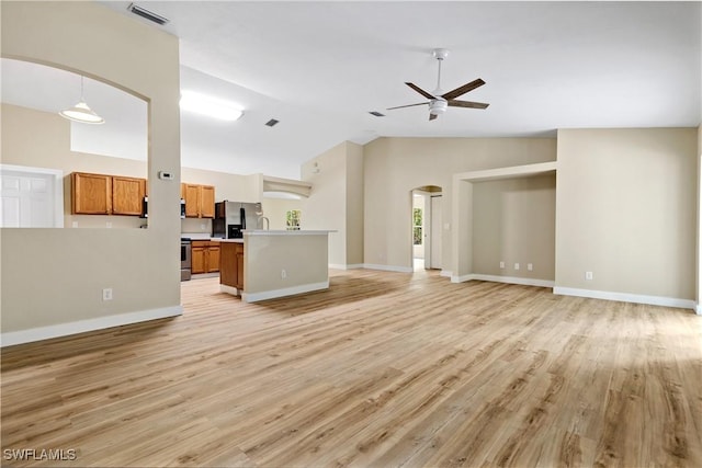 unfurnished living room featuring visible vents, light wood-style flooring, arched walkways, baseboards, and ceiling fan