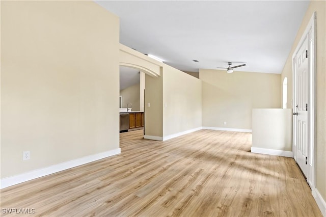 spare room featuring light wood-style flooring, a ceiling fan, baseboards, and arched walkways