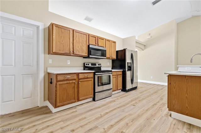 kitchen with brown cabinetry, visible vents, light wood-style flooring, light countertops, and appliances with stainless steel finishes