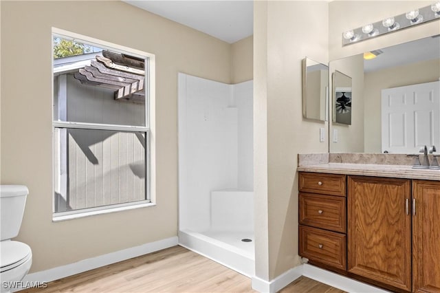 bathroom with toilet, wood finished floors, baseboards, walk in shower, and vanity