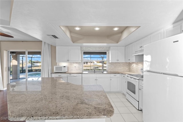 kitchen featuring decorative backsplash, light stone countertops, white appliances, a tray ceiling, and white cabinets