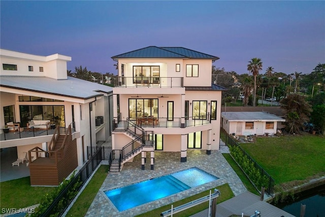 back house at dusk with a balcony, a fenced in pool, a patio, and a yard