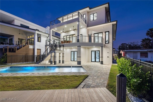 back house at night featuring a lawn, a fenced in pool, ceiling fan, a balcony, and a patio area