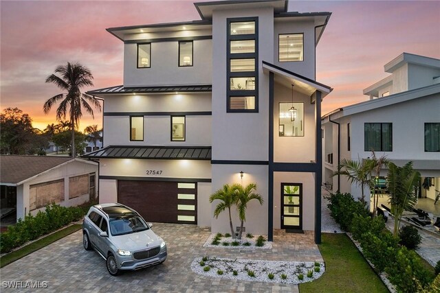 contemporary house with a garage, a standing seam roof, metal roof, and decorative driveway