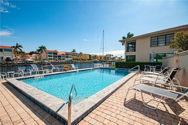 community pool with a patio, fence, and a water view