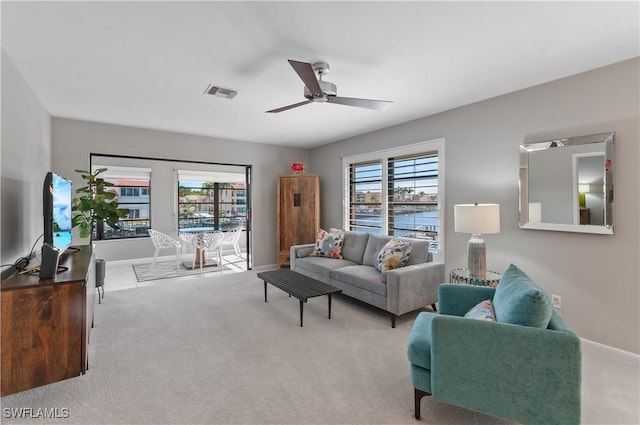 living room with ceiling fan, light colored carpet, and a water view