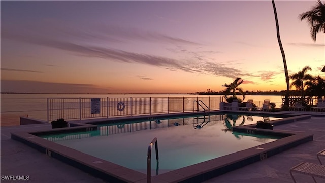 pool at dusk featuring a water view and a patio area