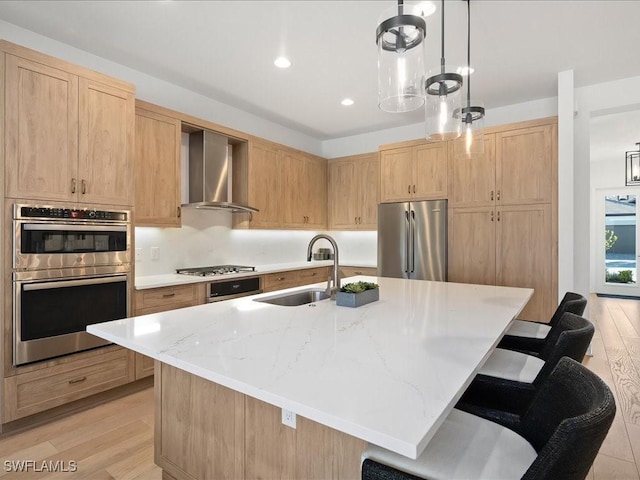 kitchen with wall chimney exhaust hood, stainless steel appliances, and an island with sink