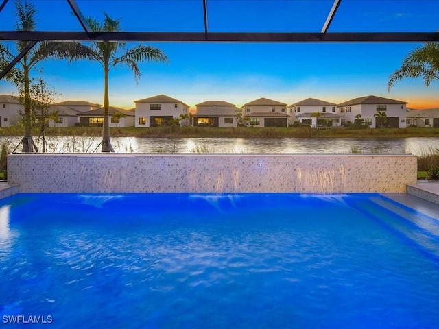 pool at dusk featuring glass enclosure and a water view