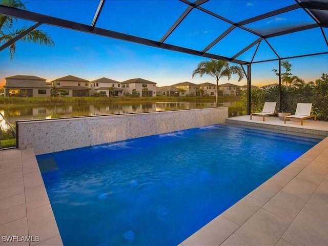 pool at dusk with pool water feature, glass enclosure, a water view, and a patio