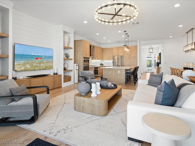 living room with built in shelves, light wood-type flooring, sink, and a chandelier