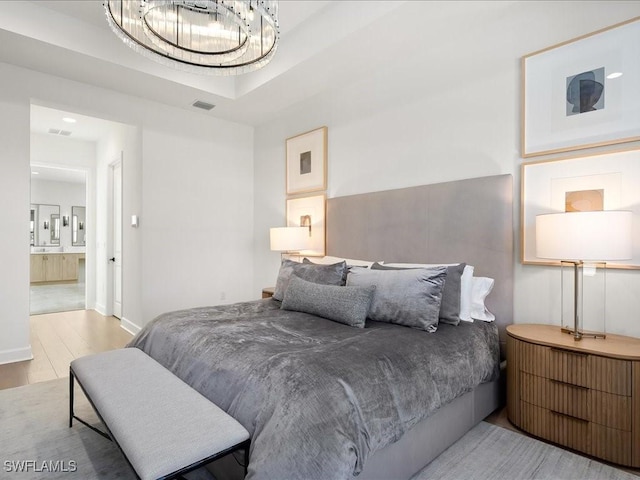 bedroom with ensuite bath, light hardwood / wood-style flooring, and a chandelier