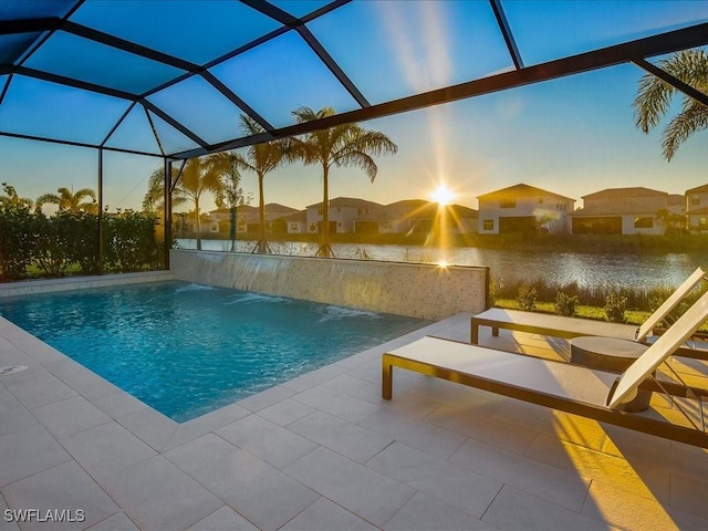 pool at dusk with a patio, pool water feature, a water view, and glass enclosure