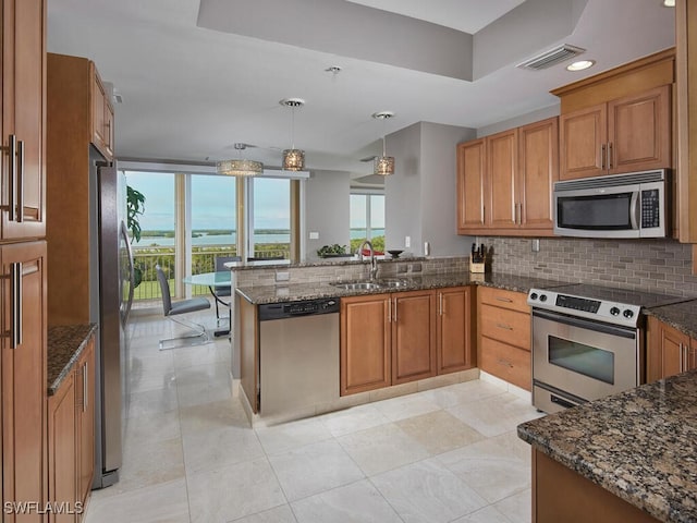 kitchen with kitchen peninsula, stainless steel appliances, sink, pendant lighting, and dark stone countertops