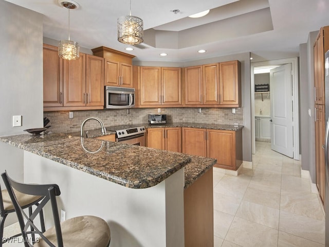 kitchen with pendant lighting, a breakfast bar area, dark stone countertops, kitchen peninsula, and stainless steel appliances