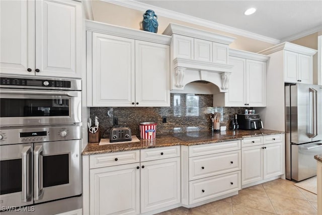 kitchen with decorative backsplash, appliances with stainless steel finishes, ornamental molding, dark stone countertops, and white cabinetry