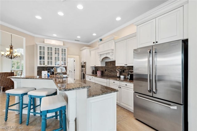 kitchen featuring white cabinets, dark stone counters, glass insert cabinets, appliances with stainless steel finishes, and a breakfast bar area