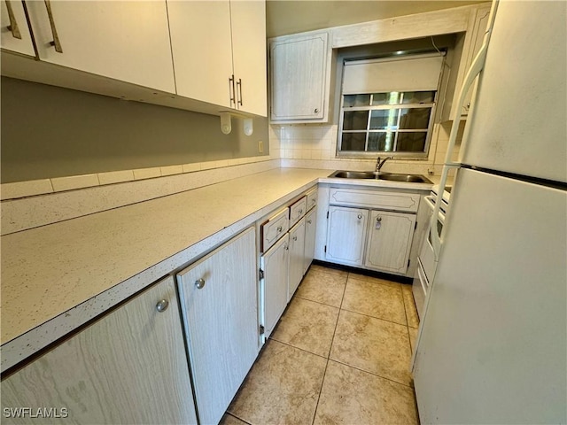 kitchen with light tile patterned floors, freestanding refrigerator, a sink, light countertops, and backsplash