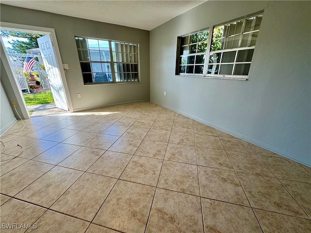 empty room featuring a textured ceiling, a textured wall, tile patterned flooring, and baseboards