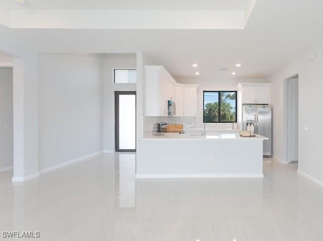 kitchen with stainless steel fridge, white cabinetry, and an island with sink