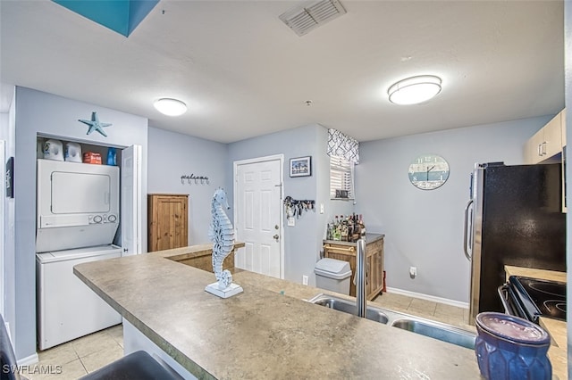 kitchen featuring light tile patterned floors, stacked washer and dryer, stainless steel refrigerator, and black / electric stove