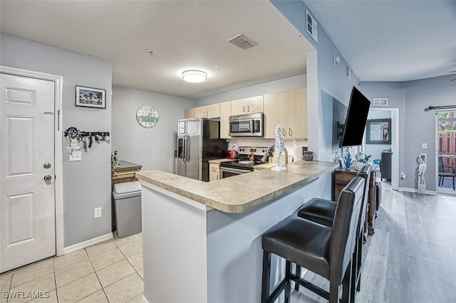 kitchen featuring light brown cabinets, a kitchen breakfast bar, kitchen peninsula, light tile patterned floors, and appliances with stainless steel finishes