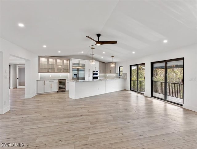 unfurnished living room featuring vaulted ceiling, sink, beverage cooler, ceiling fan, and light hardwood / wood-style flooring