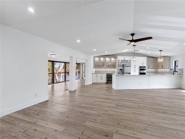 unfurnished living room with lofted ceiling, a wealth of natural light, beverage cooler, and light wood-type flooring