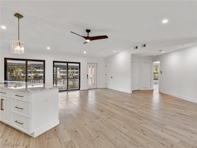 unfurnished living room featuring lofted ceiling, ceiling fan with notable chandelier, a wealth of natural light, and light wood-type flooring