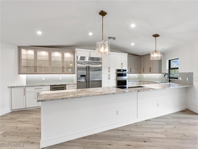 kitchen with appliances with stainless steel finishes, pendant lighting, lofted ceiling, white cabinets, and kitchen peninsula