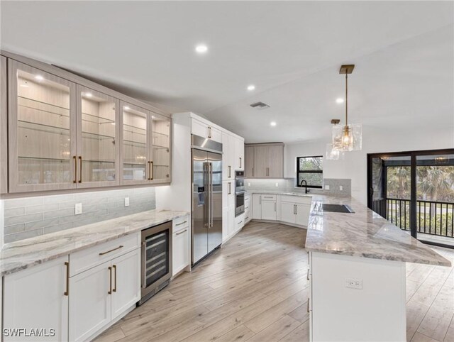 kitchen with white cabinets, hanging light fixtures, a kitchen island, wine cooler, and appliances with stainless steel finishes