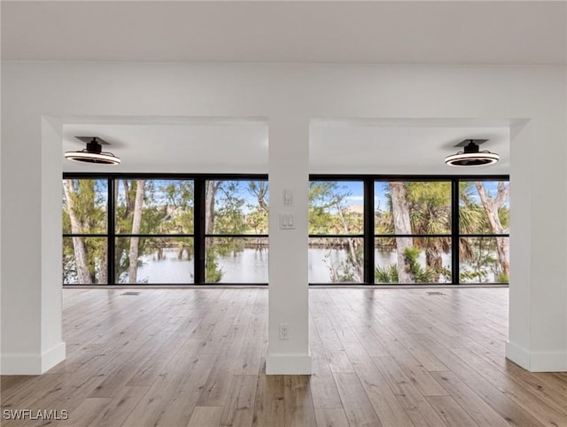 unfurnished room featuring a water view, a wall of windows, ceiling fan, and light hardwood / wood-style floors