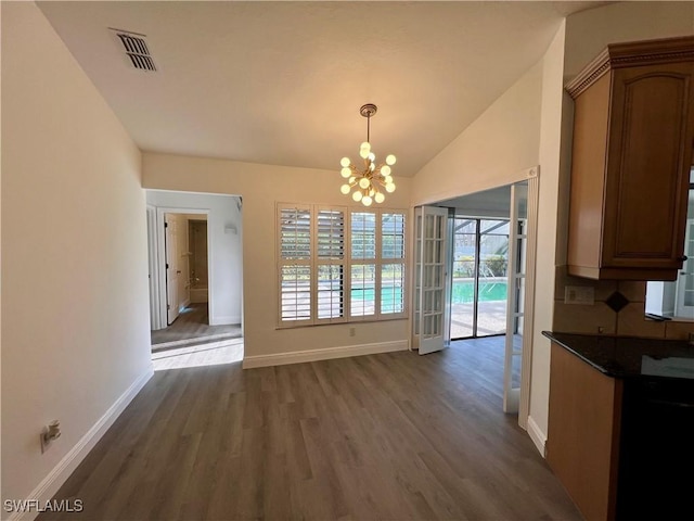 unfurnished dining area featuring dark hardwood / wood-style flooring, an inviting chandelier, and vaulted ceiling