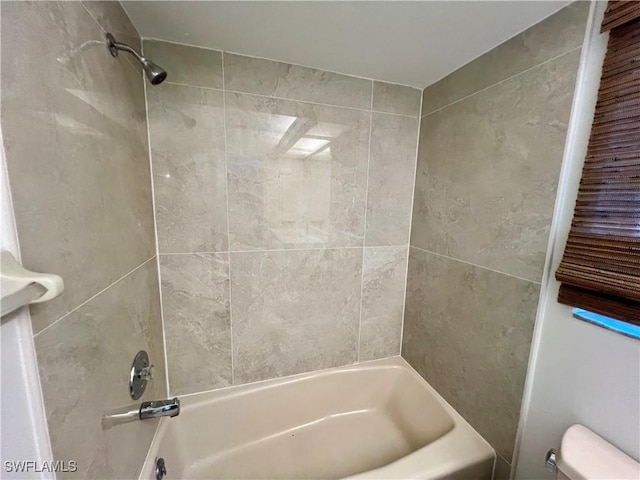 bathroom featuring tiled shower / bath combo and toilet