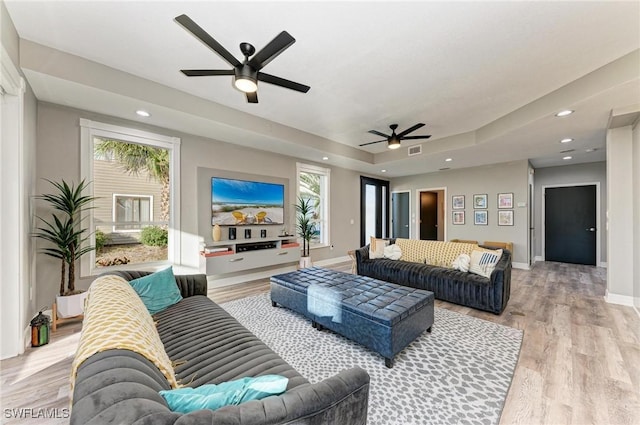 living room with light wood-type flooring, a tray ceiling, and ceiling fan