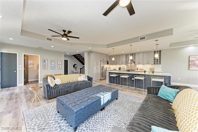 living room with light wood-type flooring, a raised ceiling, ceiling fan, and sink