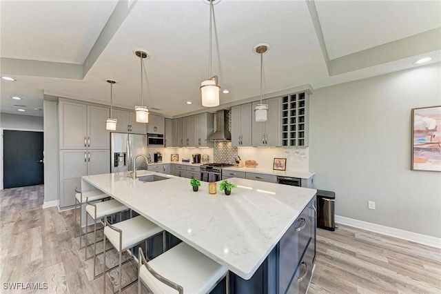 kitchen featuring sink, wall chimney exhaust hood, hanging light fixtures, stainless steel appliances, and a large island with sink