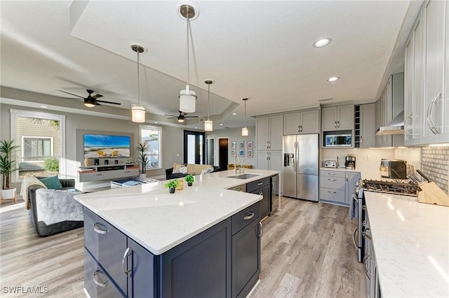 kitchen with a spacious island, sink, ceiling fan, light stone countertops, and appliances with stainless steel finishes