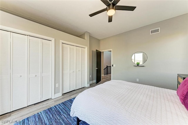 bedroom featuring hardwood / wood-style floors, ceiling fan, and multiple closets