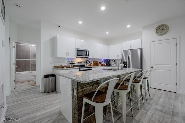 kitchen with sink, stainless steel appliances, a kitchen bar, a center island with sink, and white cabinets