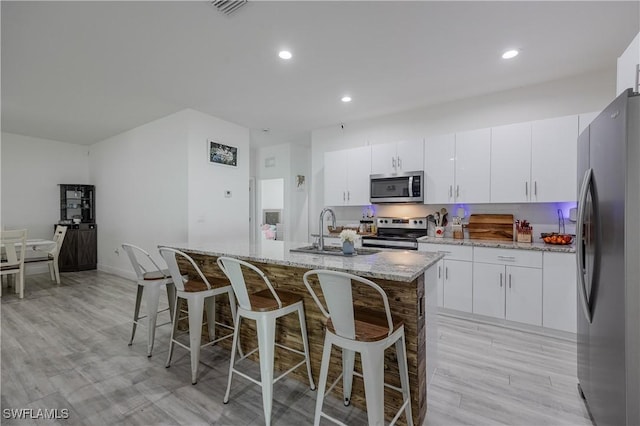 kitchen featuring light stone counters, stainless steel appliances, white cabinetry, and an island with sink