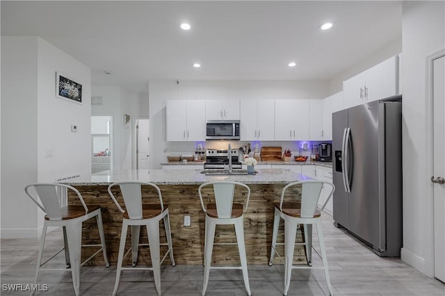 kitchen featuring light stone counters, a breakfast bar, white cabinets, and appliances with stainless steel finishes