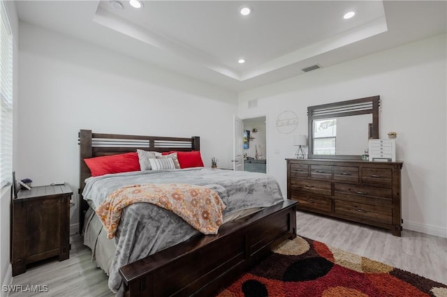 bedroom with a raised ceiling and light wood-type flooring