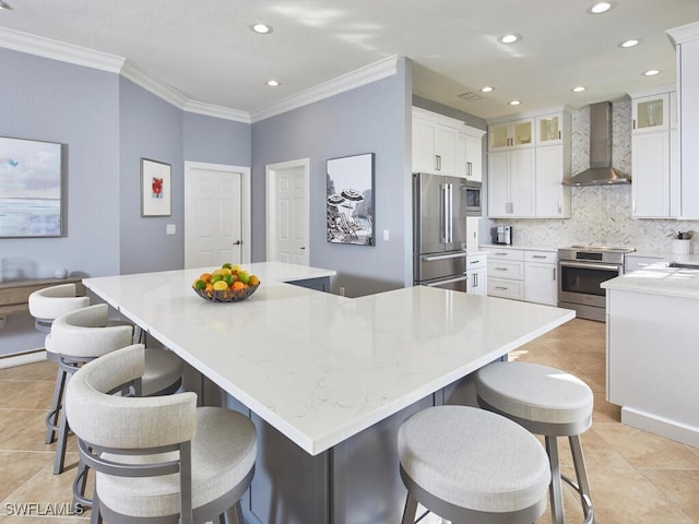 kitchen featuring appliances with stainless steel finishes, white cabinetry, a spacious island, and wall chimney range hood