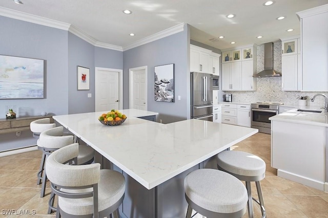 kitchen with tasteful backsplash, wall chimney range hood, ornamental molding, appliances with stainless steel finishes, and white cabinets