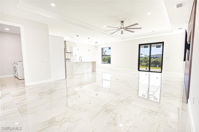 spare room with ceiling fan, sink, crown molding, a tray ceiling, and washer and clothes dryer