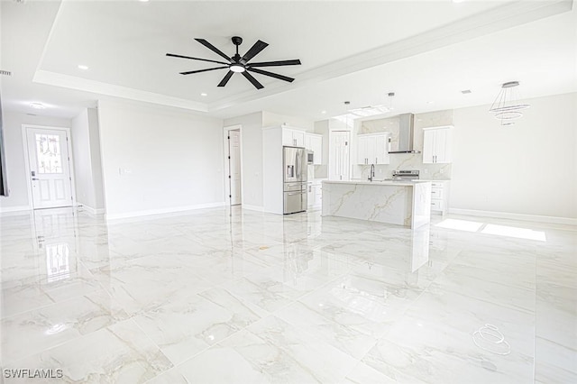 unfurnished living room with ceiling fan, ornamental molding, sink, and a tray ceiling