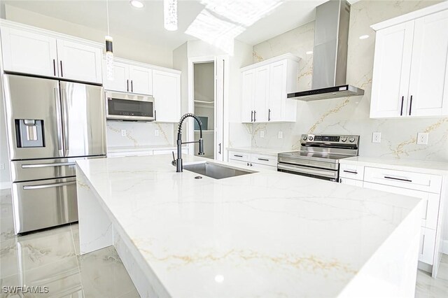 kitchen with light stone countertops, sink, stainless steel appliances, wall chimney range hood, and white cabinets